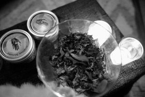 A black and white close-up of mason jars and scattered herbs on a table surface.