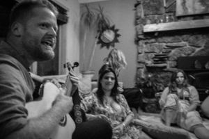 A casual gathering in a living room with stone fireplace showing people engaged in conversation.