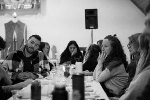 Candid black and white photo capturing animated conversation and laughter during a social gathering.