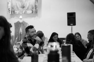 A black and white candid photo of a social gathering with people seated around a table during a dinner event.