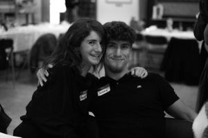 A black and white photo of two people embracing at a social event wearing name tags.