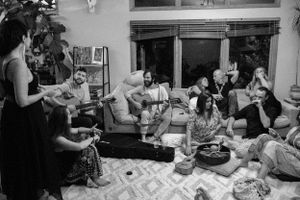 Friends gather around guitars and drinks for a cozy indoor musical evening.