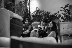 People sit and watch attentively in a room filled with houseplants.