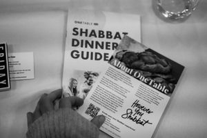 A black and white photograph showing a Shabbat dinner guide on a white tablecloth.