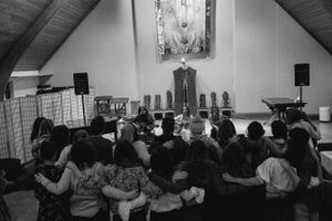 Black and white photo of a crowded indoor gathering with people seated facing a wall with decorations.
