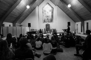 A church or chapel interior with people seated on the floor during an event.