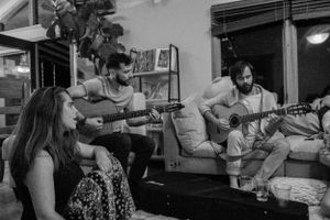 Musicians with acoustic guitars perform during an intimate living room concert.