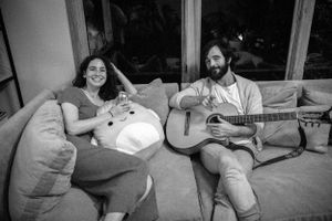 Two people relax on a couch while one plays acoustic guitar in a casual setting.