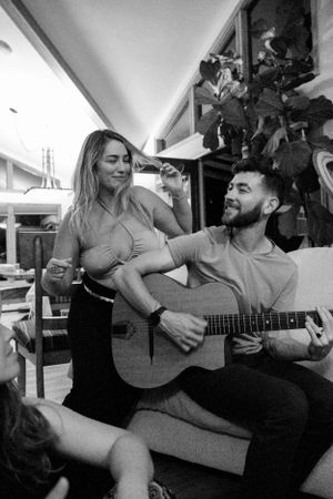 A couple shares a musical moment with an acoustic guitar in a casual indoor setting.
