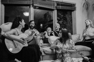 A group enjoys music together as someone plays acoustic guitar in a casual indoor setting.