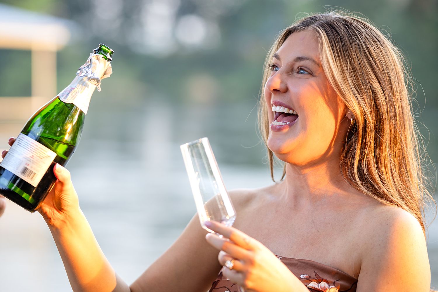 Bride smiles holding champagne and glass after engagement by the White River in Cotter, Arkansas.