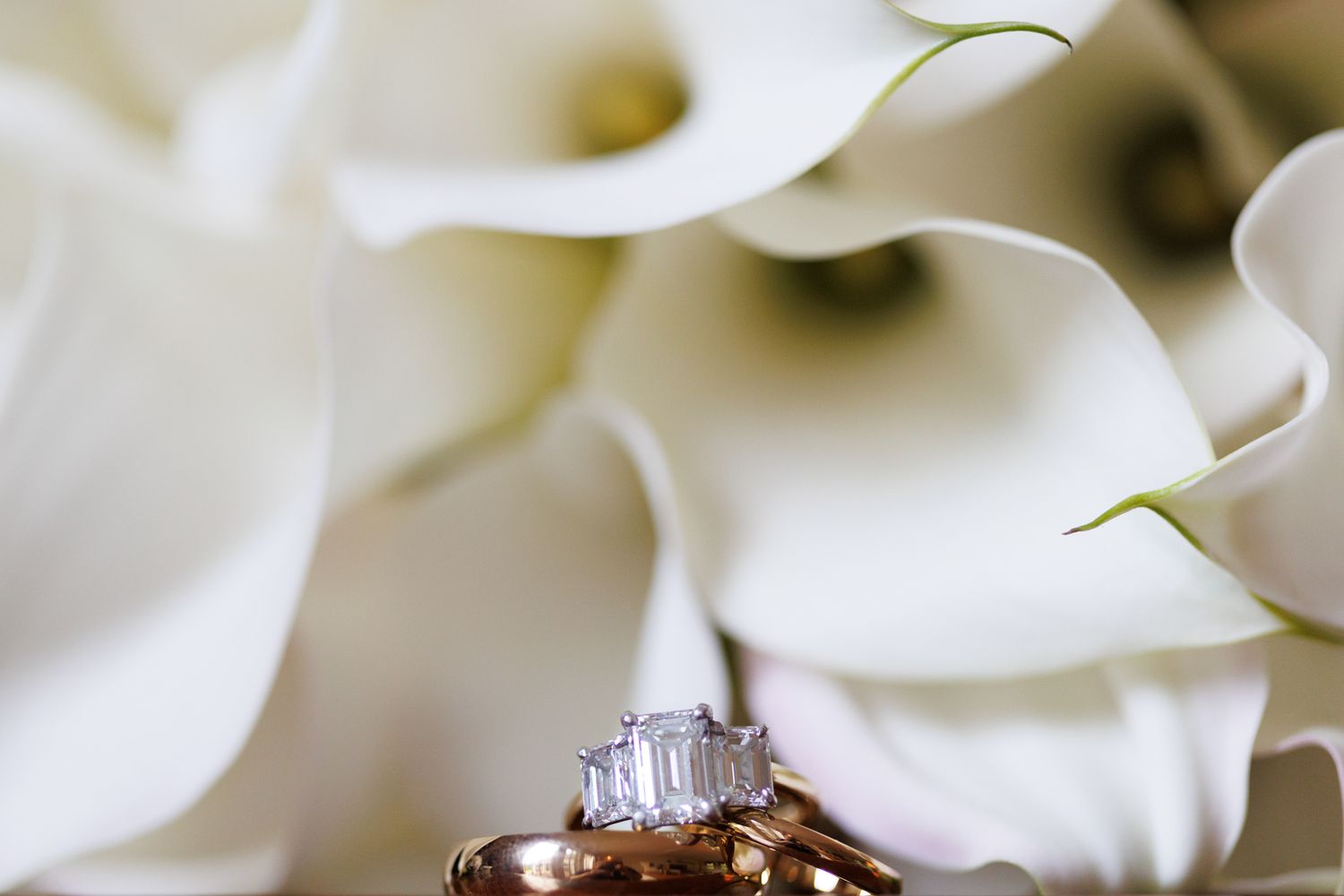Close-up of an elegant diamond engagement ring nestled among white calla lily petals.