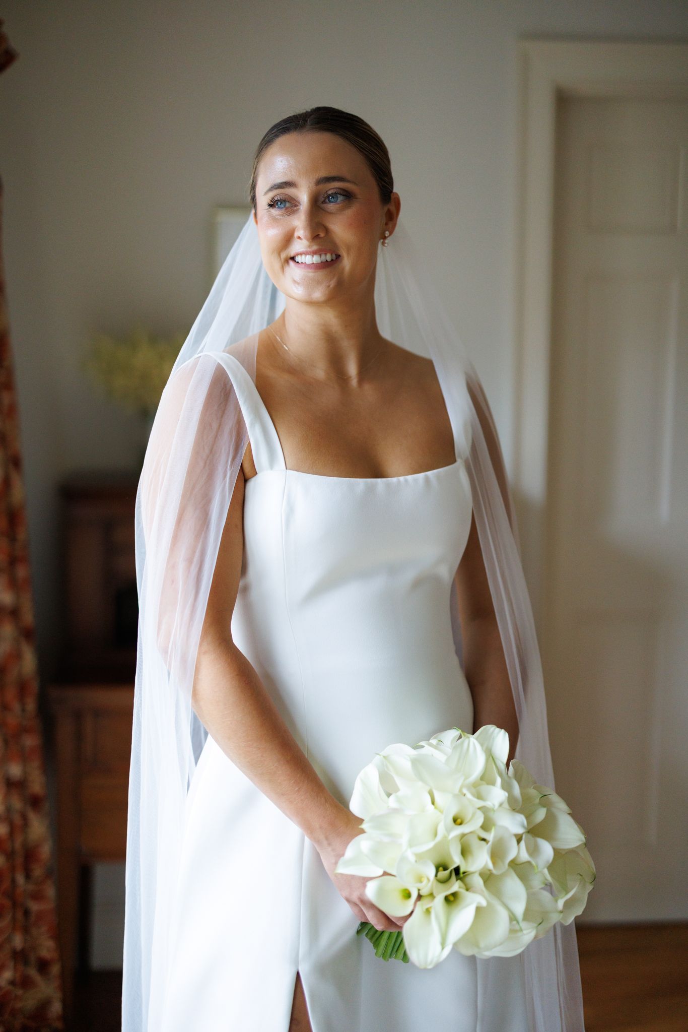 Elegant bride in sleeveless white gown holding a bouquet of white calla lilies.