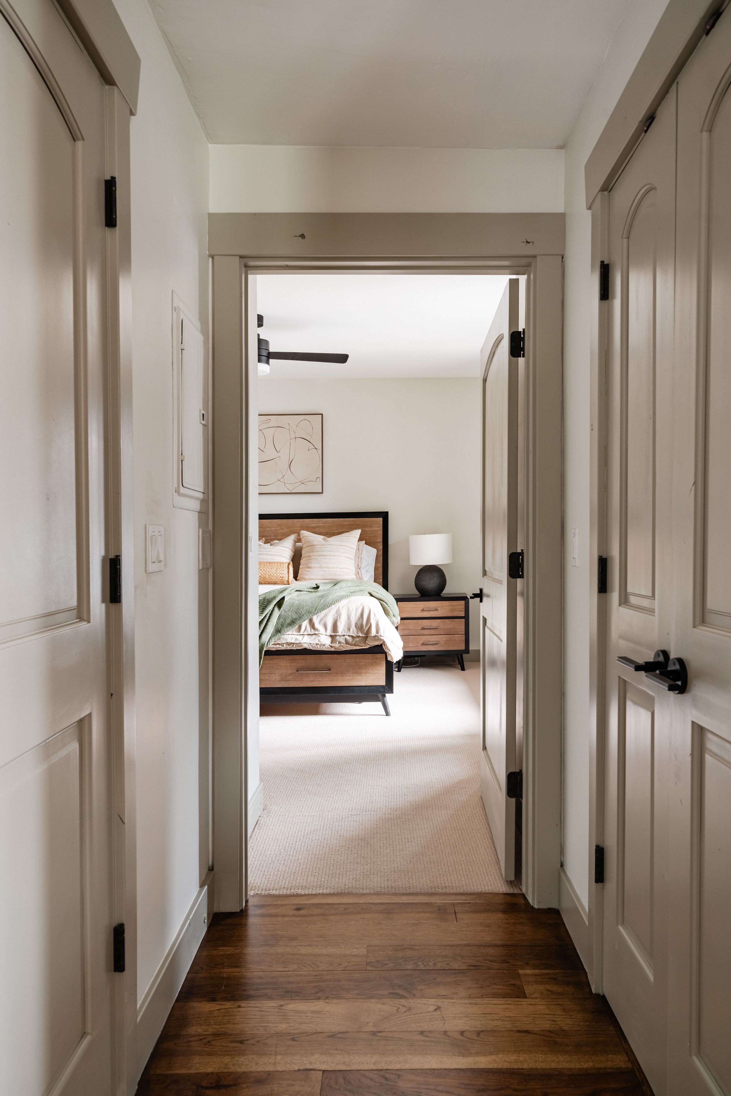 Long hallway with white walls, wooden floors, and black door hardware creates a minimalist interior design aesthetic.