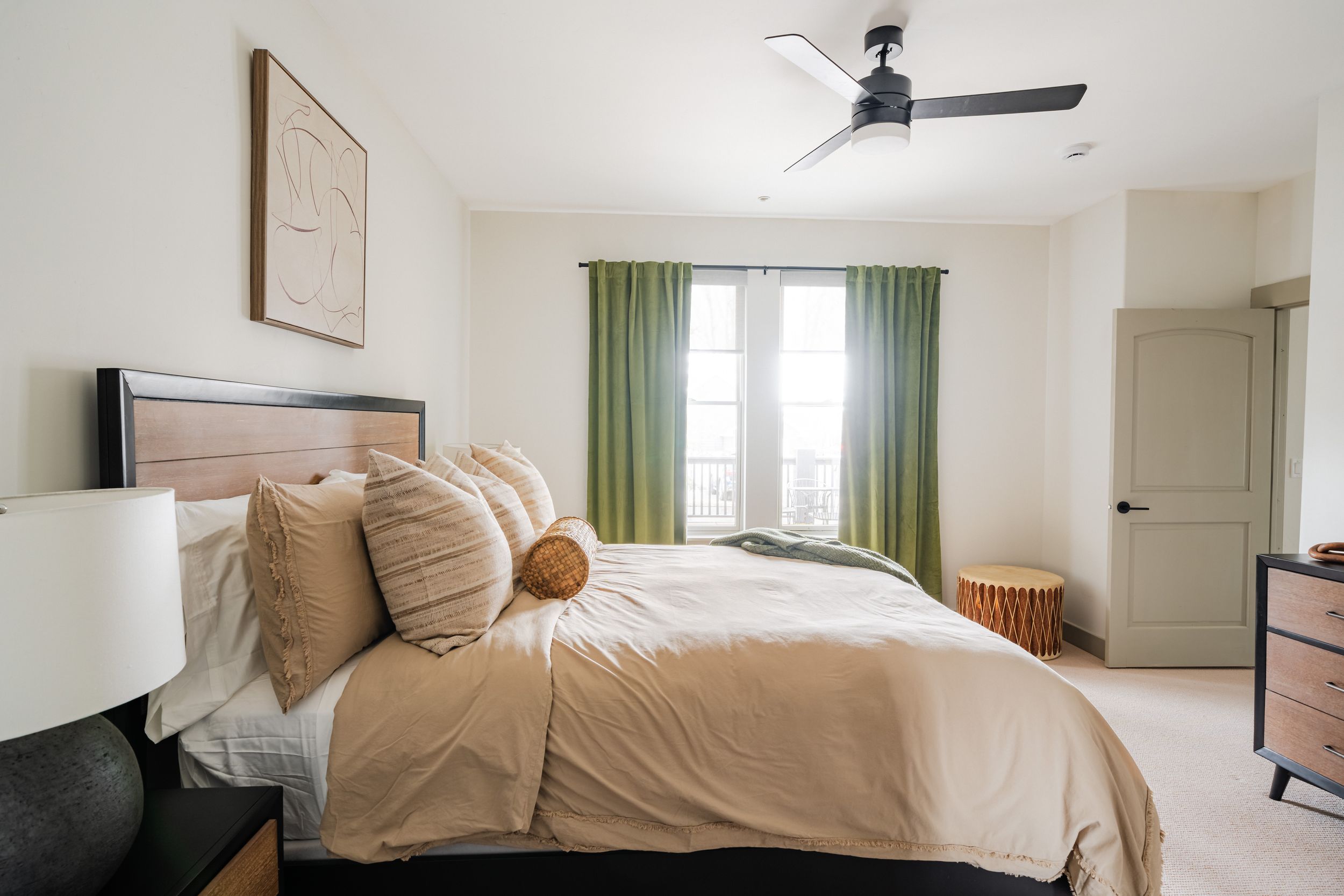 Spacious bedroom with a ceiling fan, green curtains, and a comfortable king-sized bed in neutral tones.