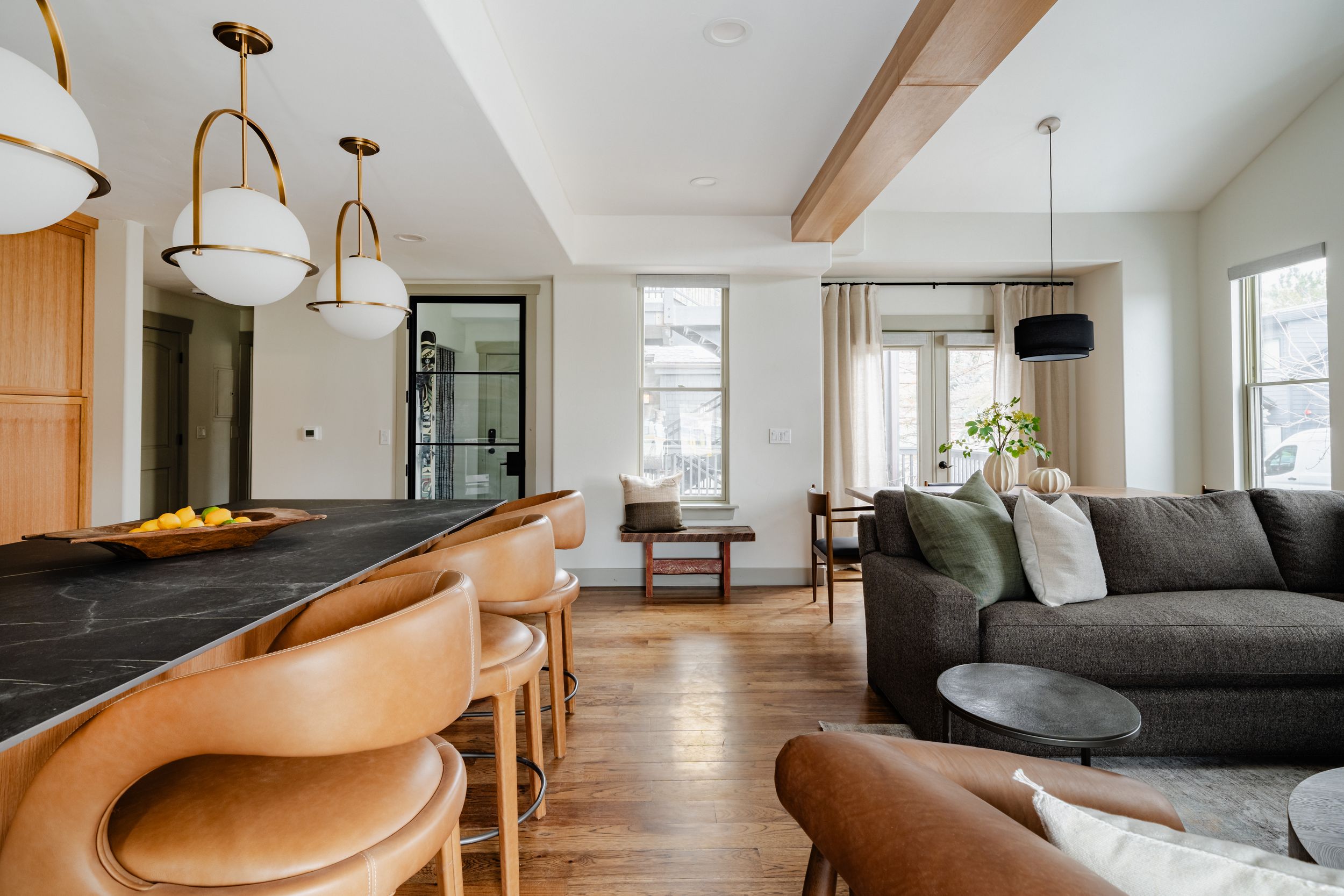 An open concept living space with wood beams, modern furniture, and contemporary light fixtures fills a bright room.