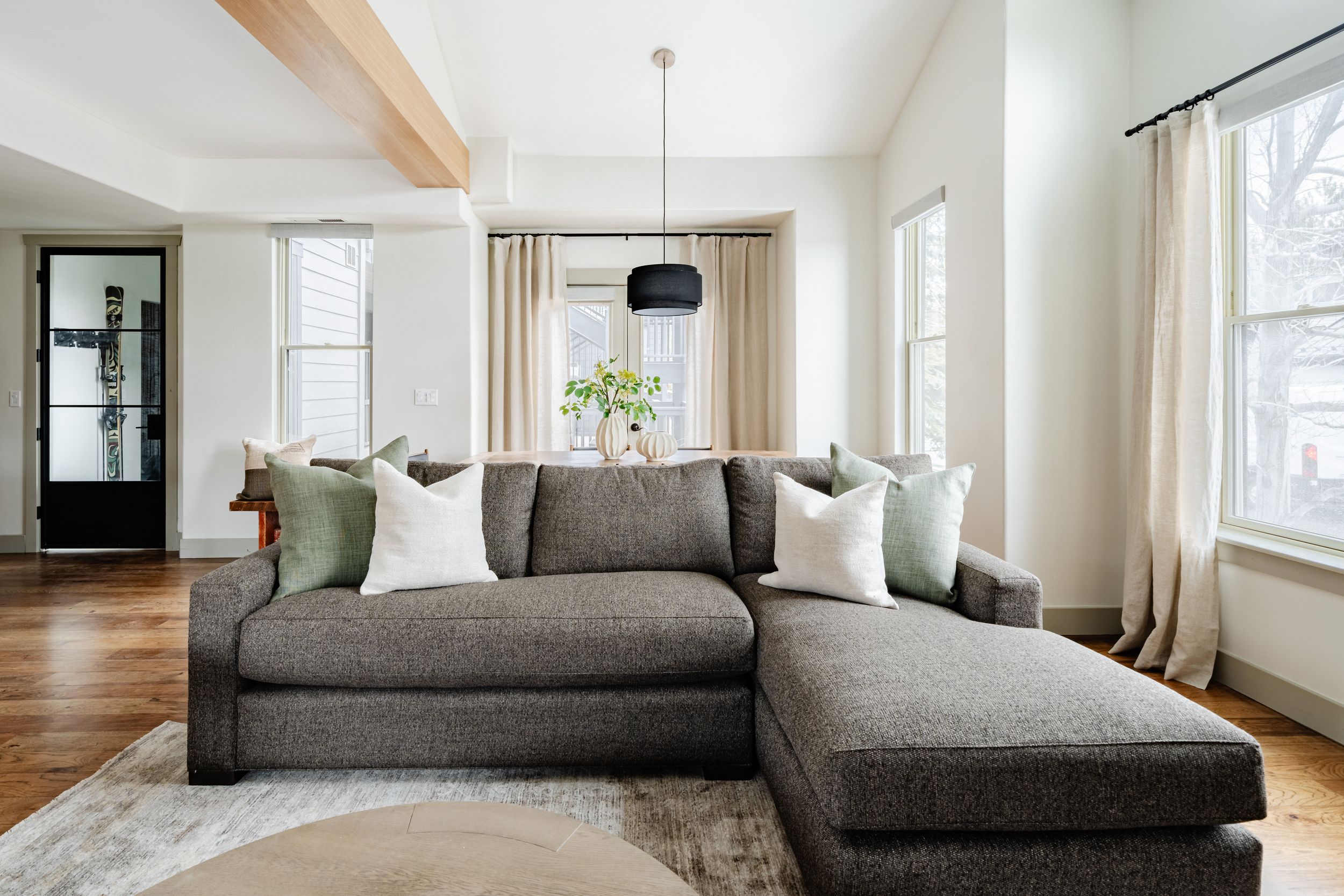 Modern living room with grey L-shaped sectional sofa, white pillows, and black display cabinet in bright natural light.