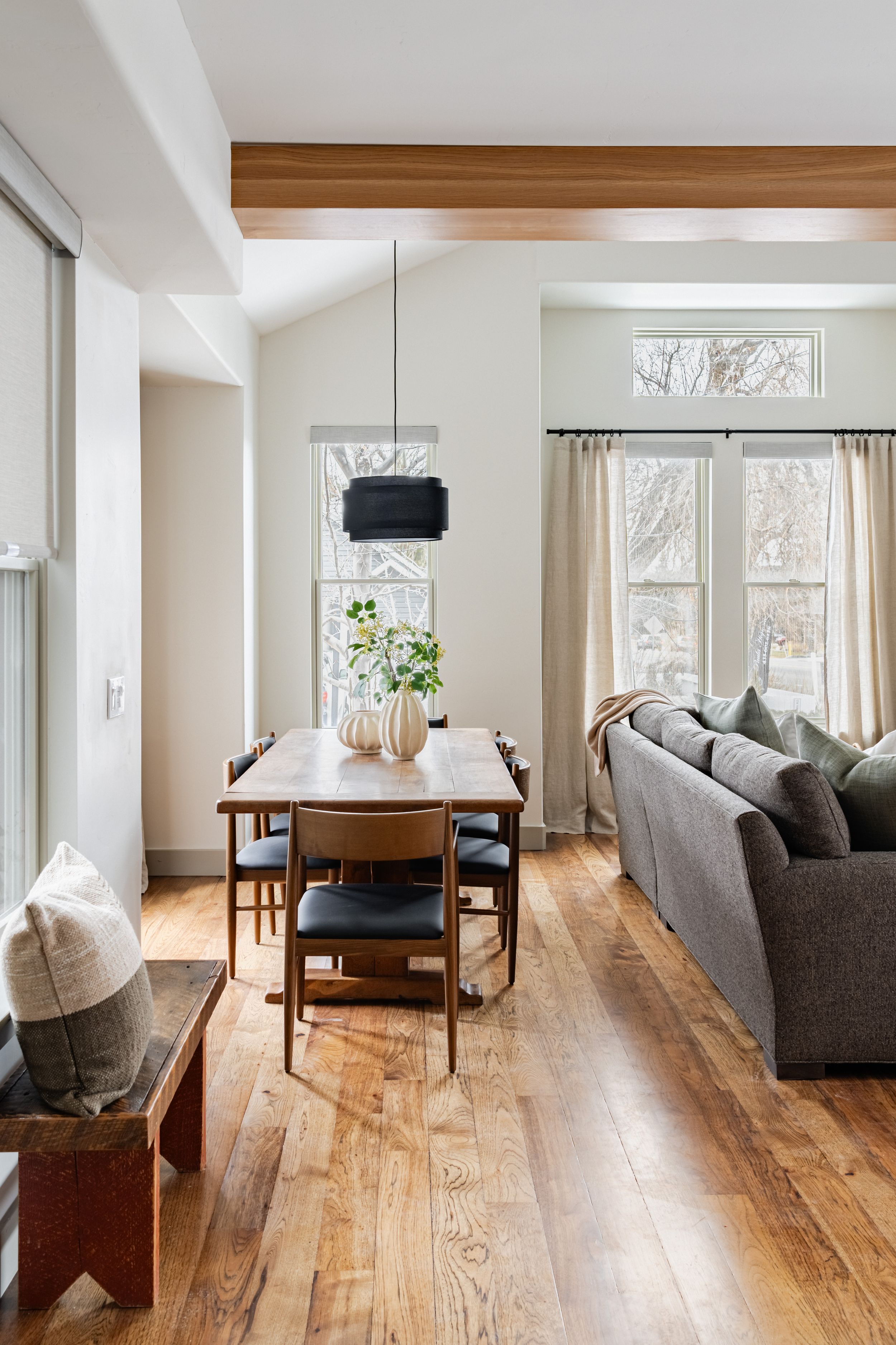 Modern minimalist living space with wooden flooring, white walls, and natural light from large windows.