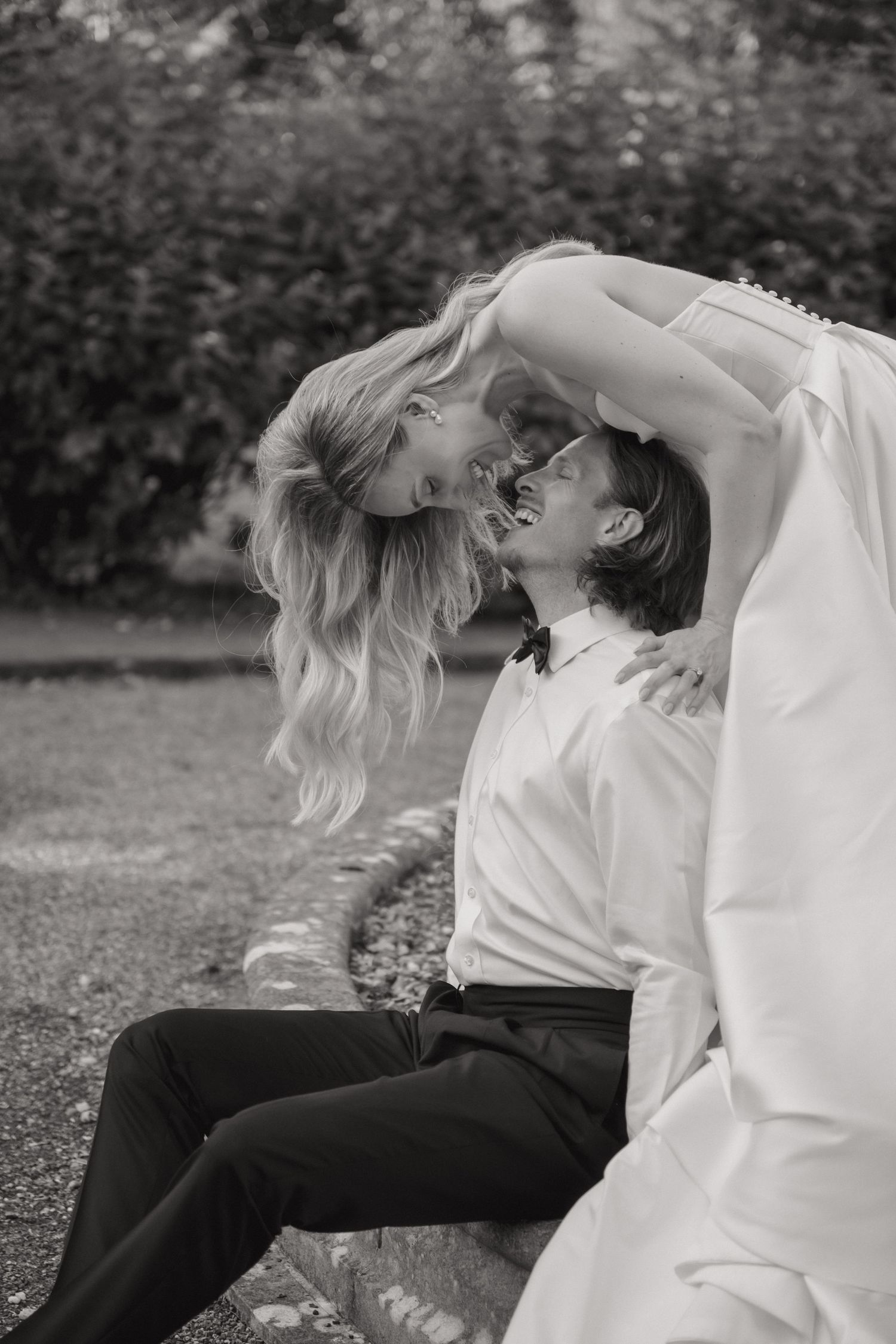 A romantic black and white wedding photo showing an intimate moment between newlyweds in a garden setting.