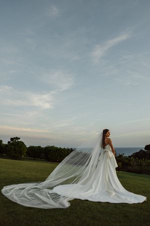 A dramatic panoramic series of wedding dress silhouettes against a sunset sky with flowing veil trailing on grass.