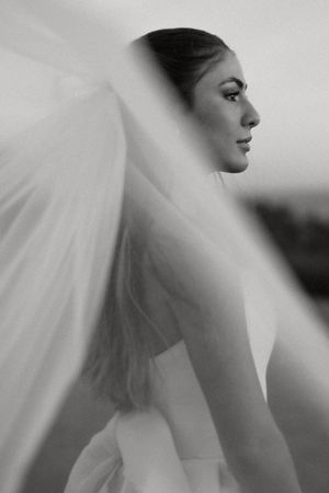 A dramatic black and white bridal portrait showing a side profile with flowing veil against blurred background.