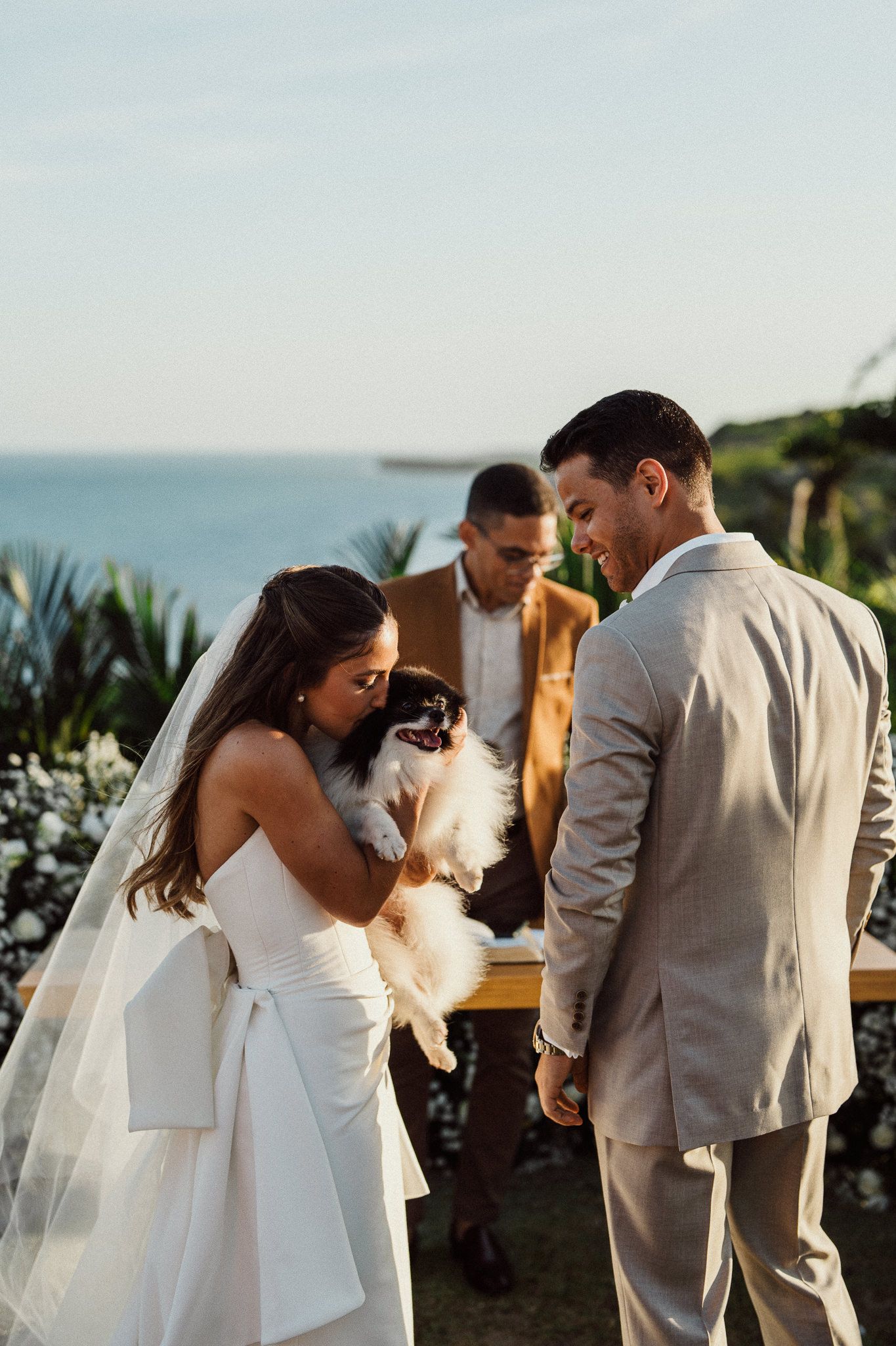 A couple shares a sweet moment with their dog during an outdoor oceanside wedding ceremony.