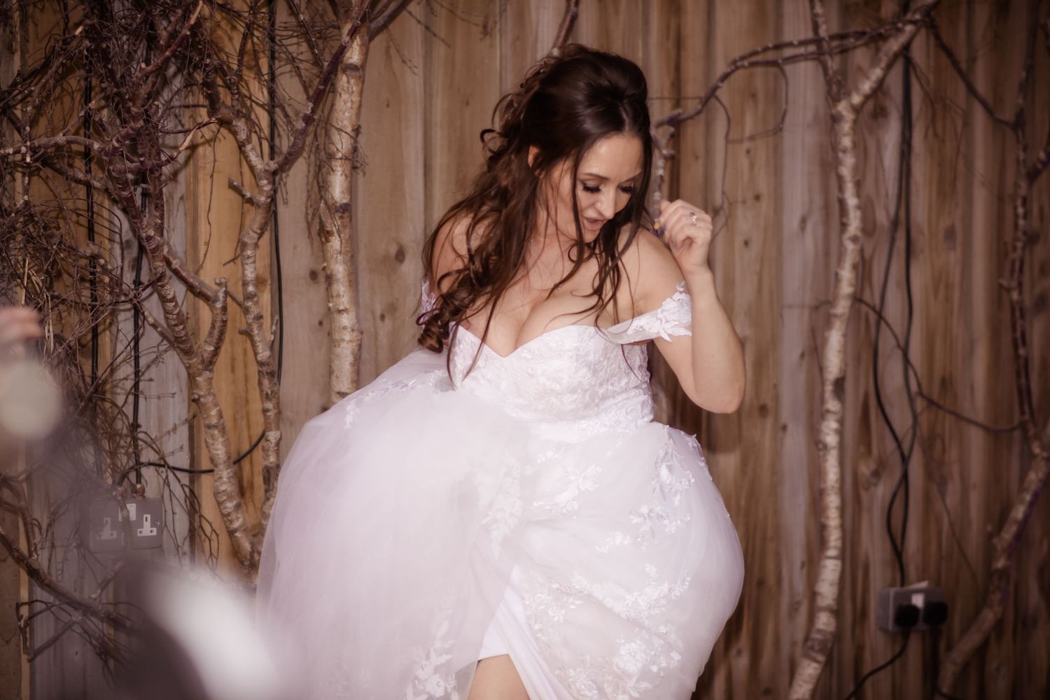 A bride in a flowing white gown twirls gracefully against a rustic wooden background.