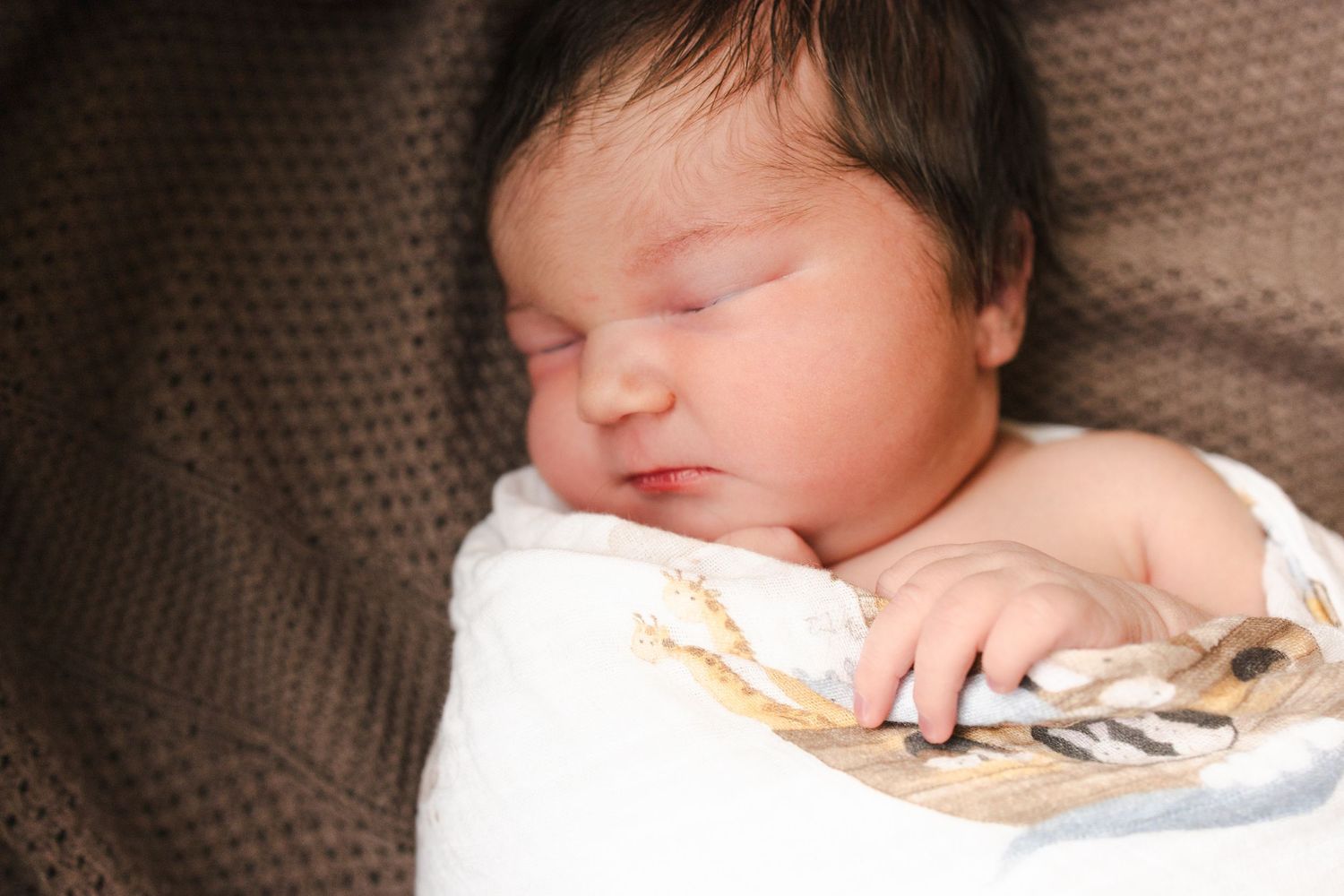 A sleeping baby rests peacefully on a brown textured blanket.