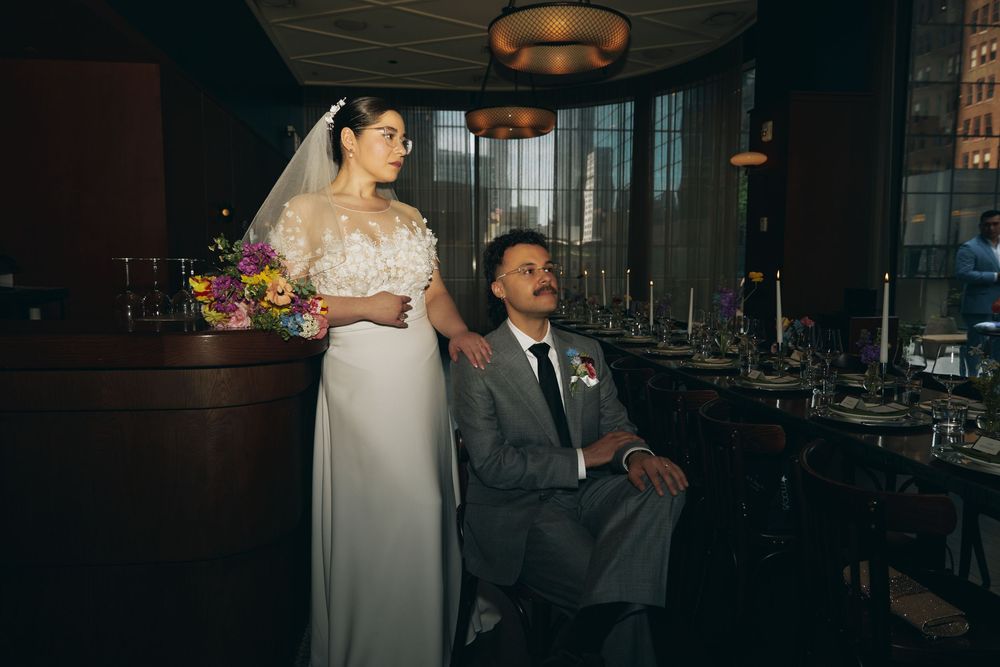 A romantic wedding portrait in a dimly lit restaurant with elegant table settings.