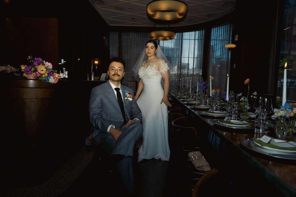Wedding couple poses in front of elegantly set dining tables in a modern restaurant space.