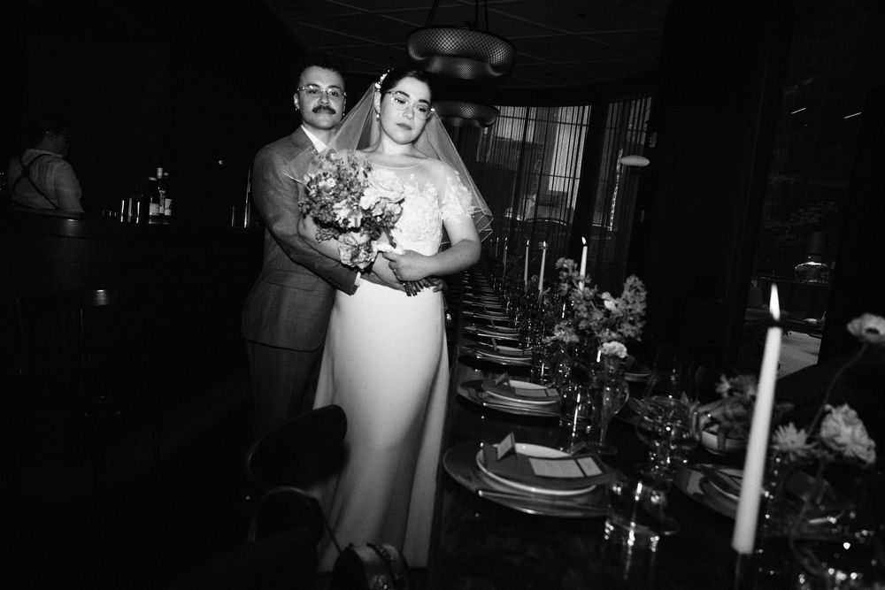 Black and white photo of a couple next to a formal dining table setting with candles and flowers.