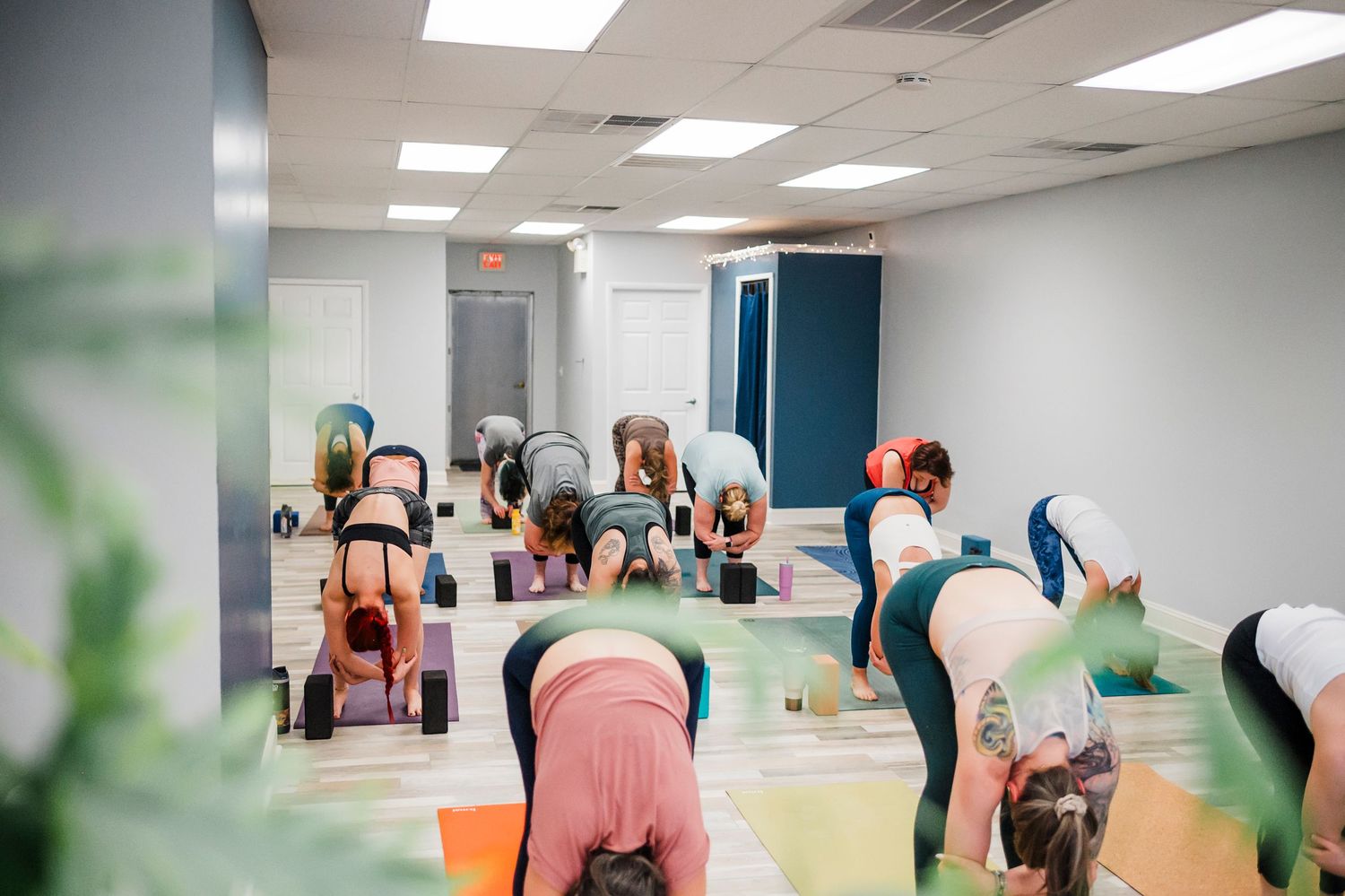 A group fitness class doing downward dog poses on colorful yoga mats in a bright studio space.