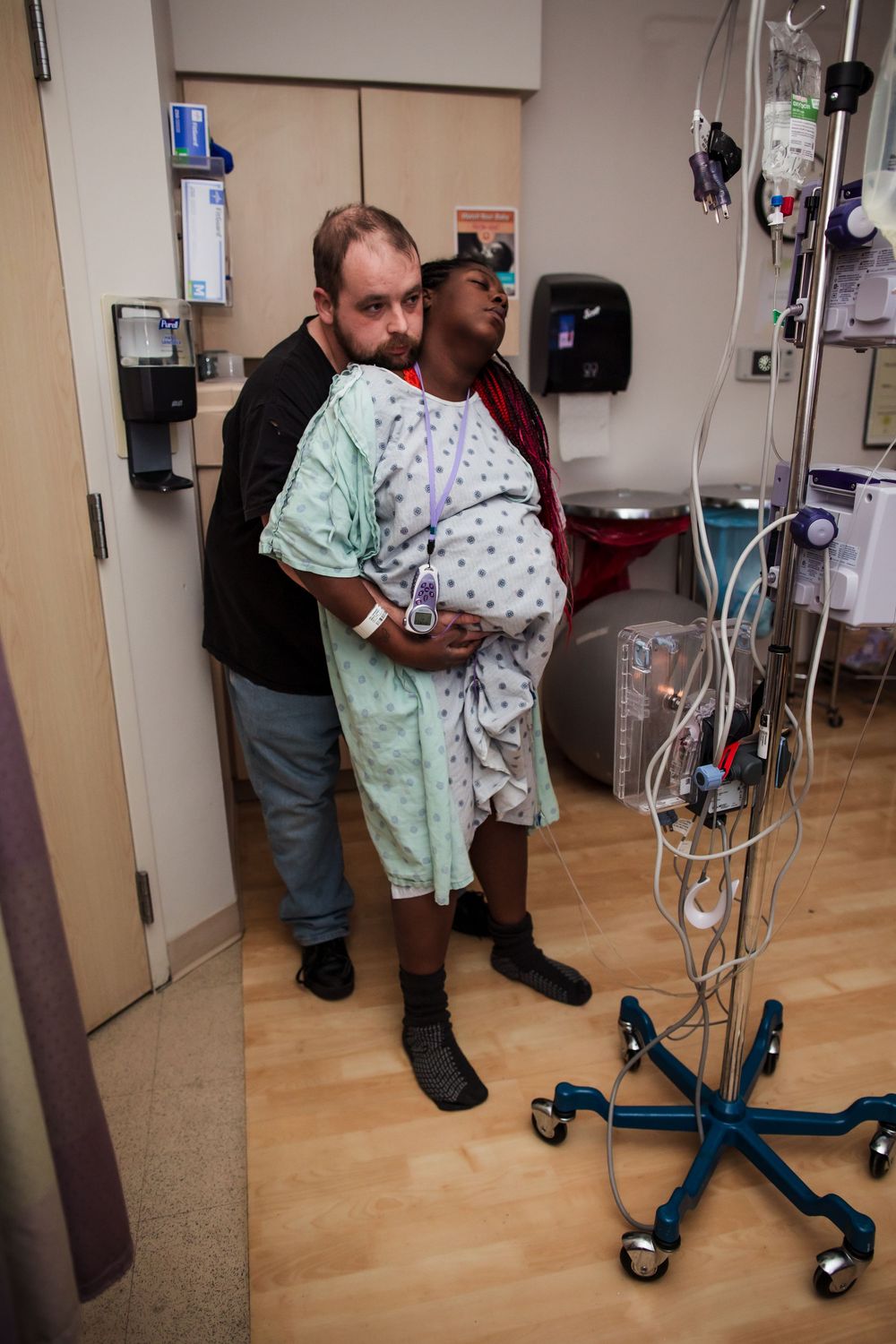 Patient using a medical walker while being supported by hospital staff in a medical facility.