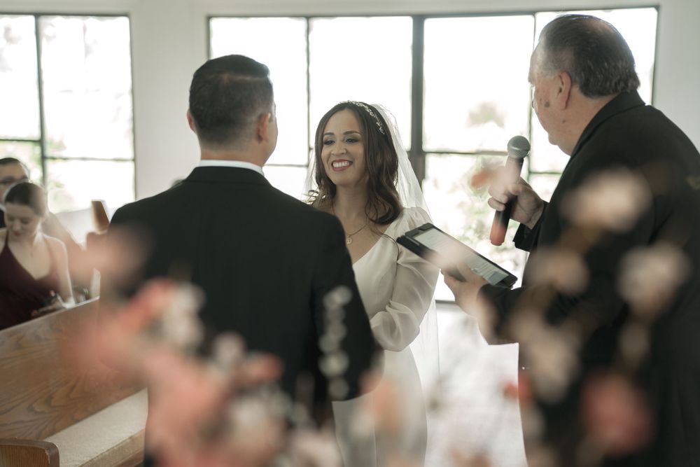 Wedding guests gathered in a bright indoor reception venue with large windows.