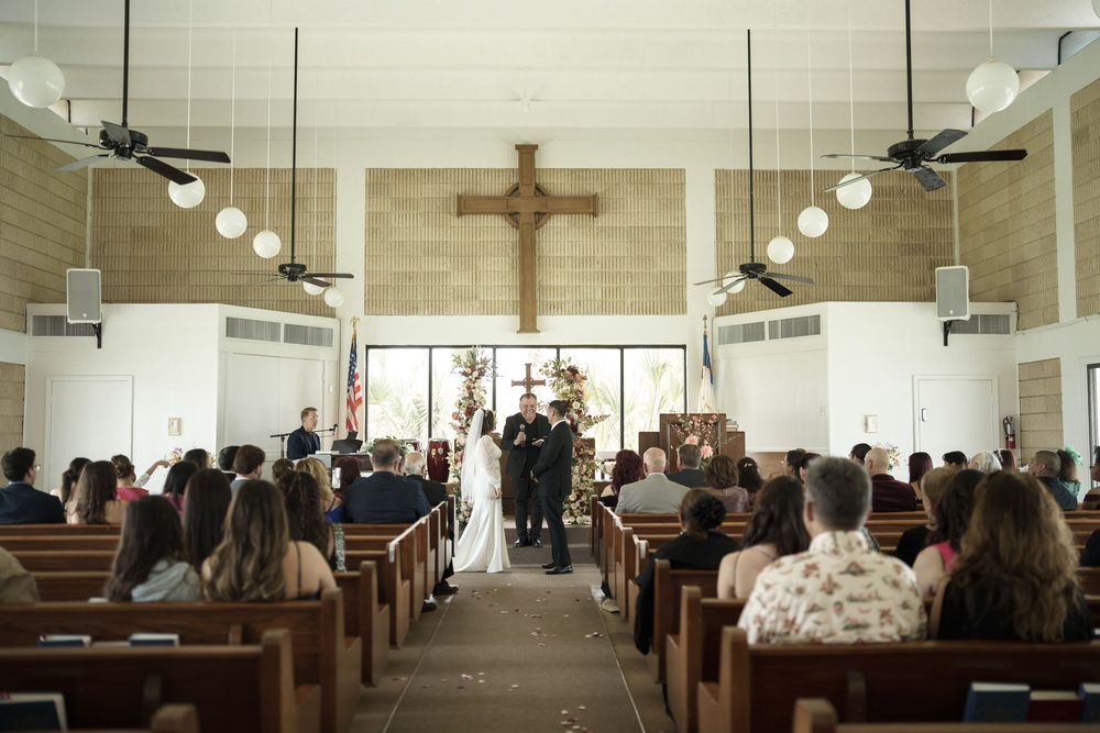 Interior of a church with wooden pews and a crucifix during a wedding ceremony.