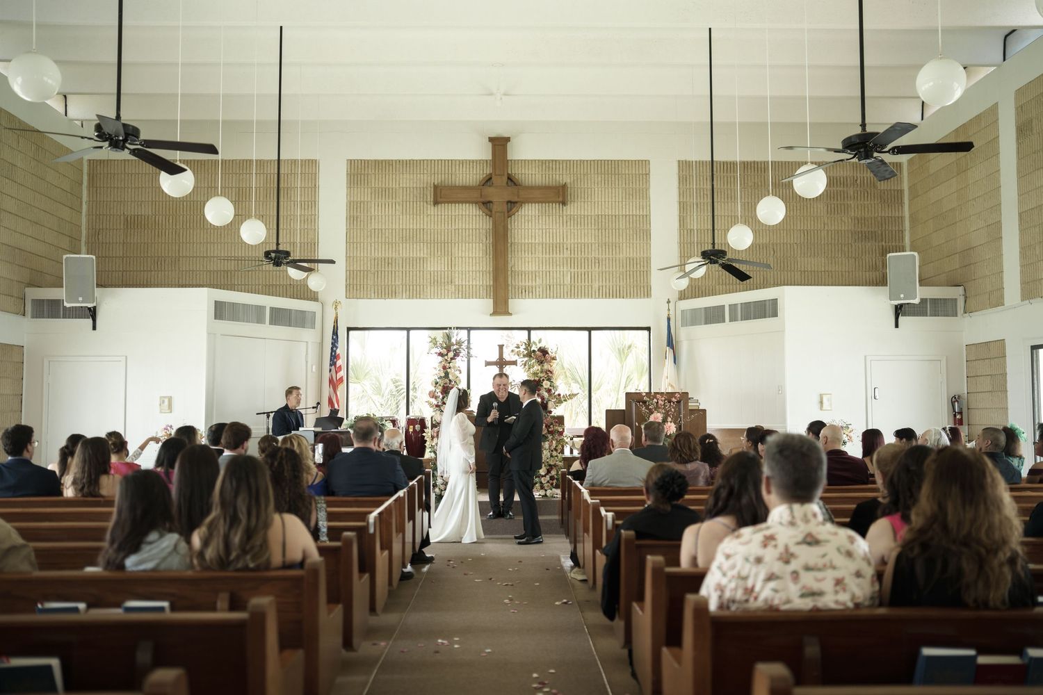Interior of a church with wooden pews and a crucifix during a wedding ceremony.
