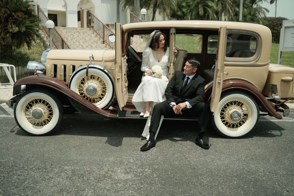 A couple sits in a classic 1930s car during their wedding photoshoot.