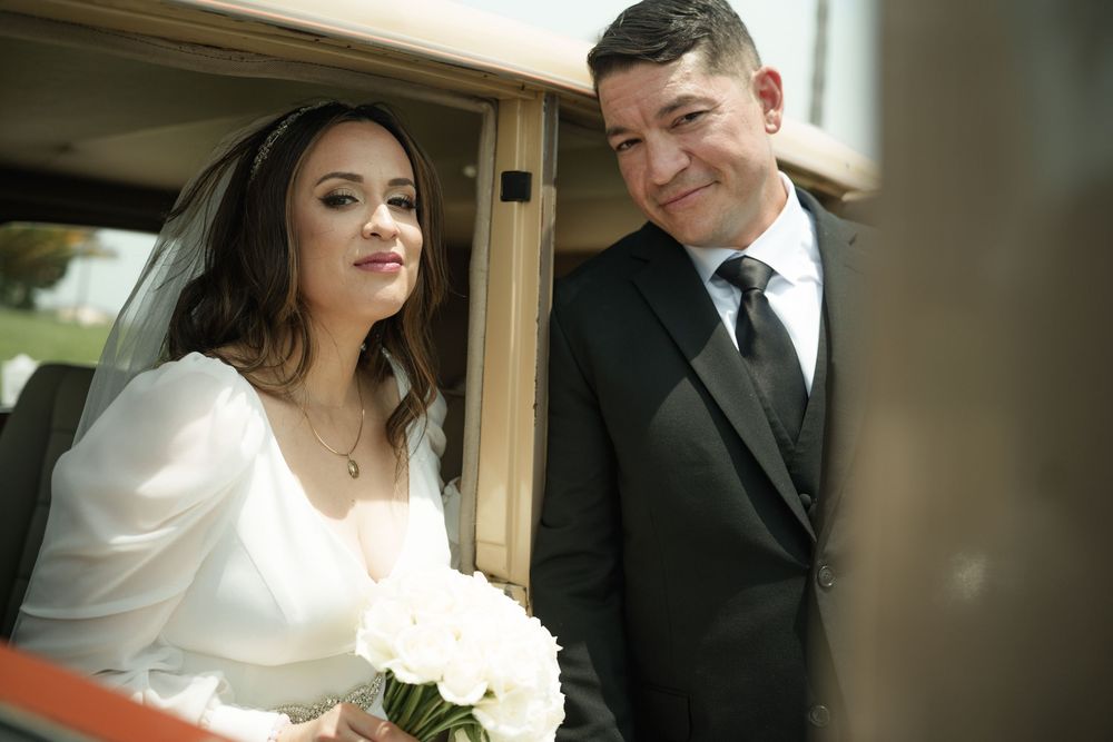 A couple shares a tender moment near their wedding transportation.