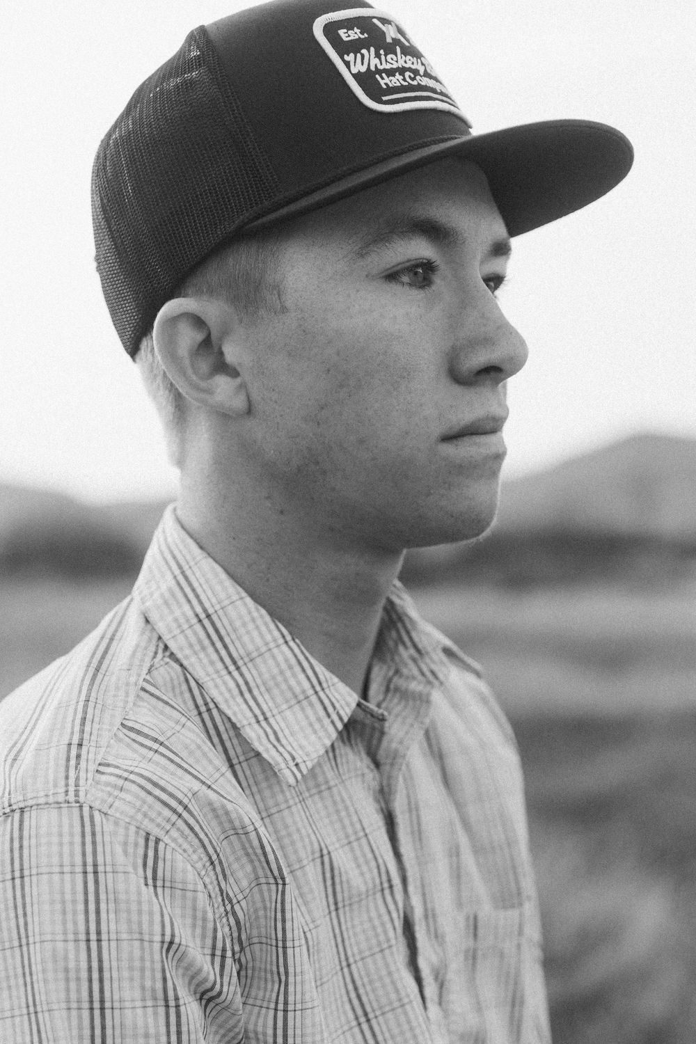 Side profile of person wearing baseball cap and plaid shirt in black and white.