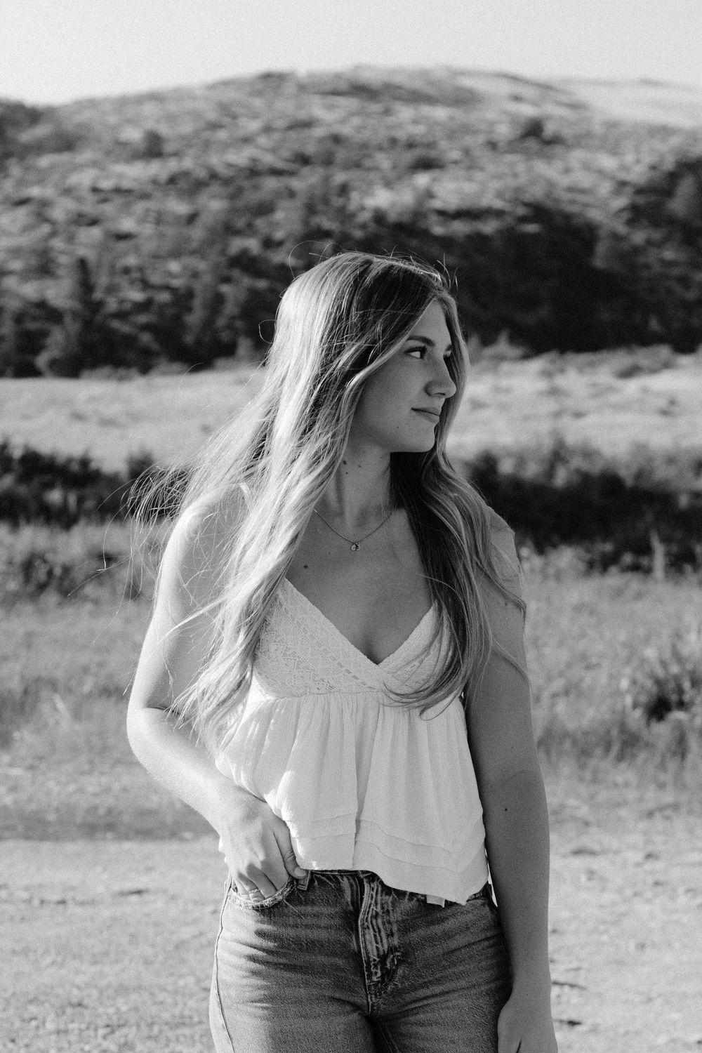 Person in white top and jeans poses in black and white against desert landscape.