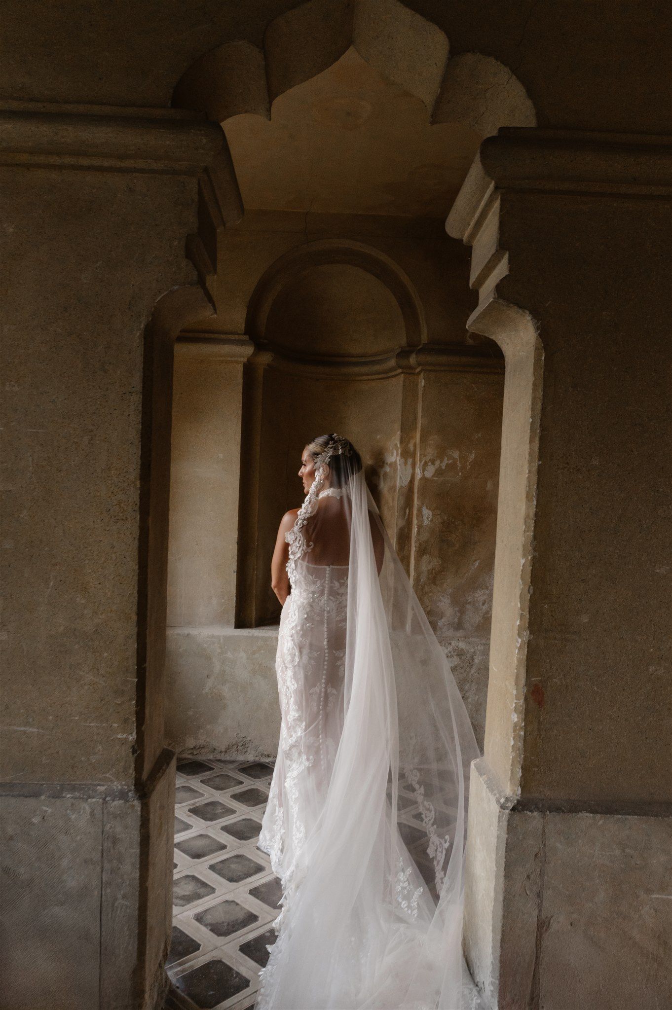 Dramatic bridal portrait in a historic stone corridor with flowing veil.