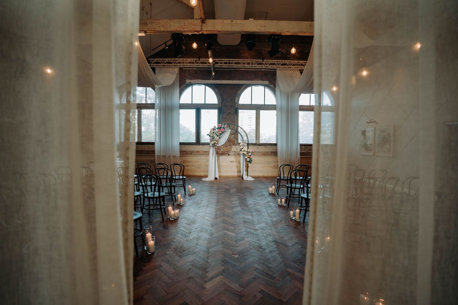 Empty wedding ceremony venue with herringbone floors and arched windows.