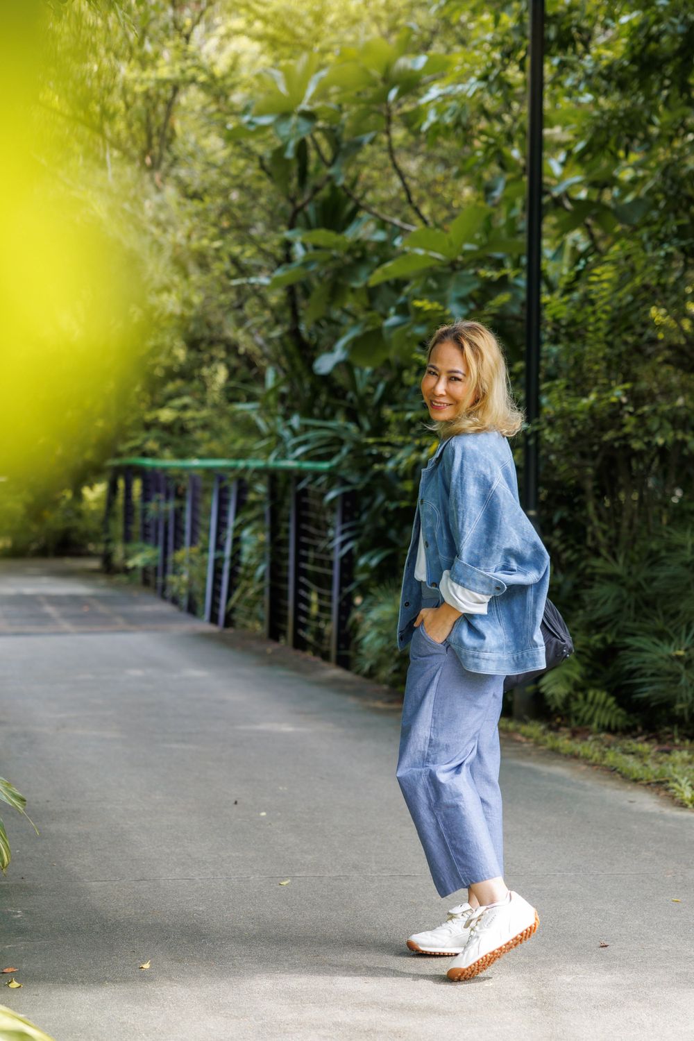 Relaxed denim-on-denim outfit with sneakers photographed against lush garden backdrop.