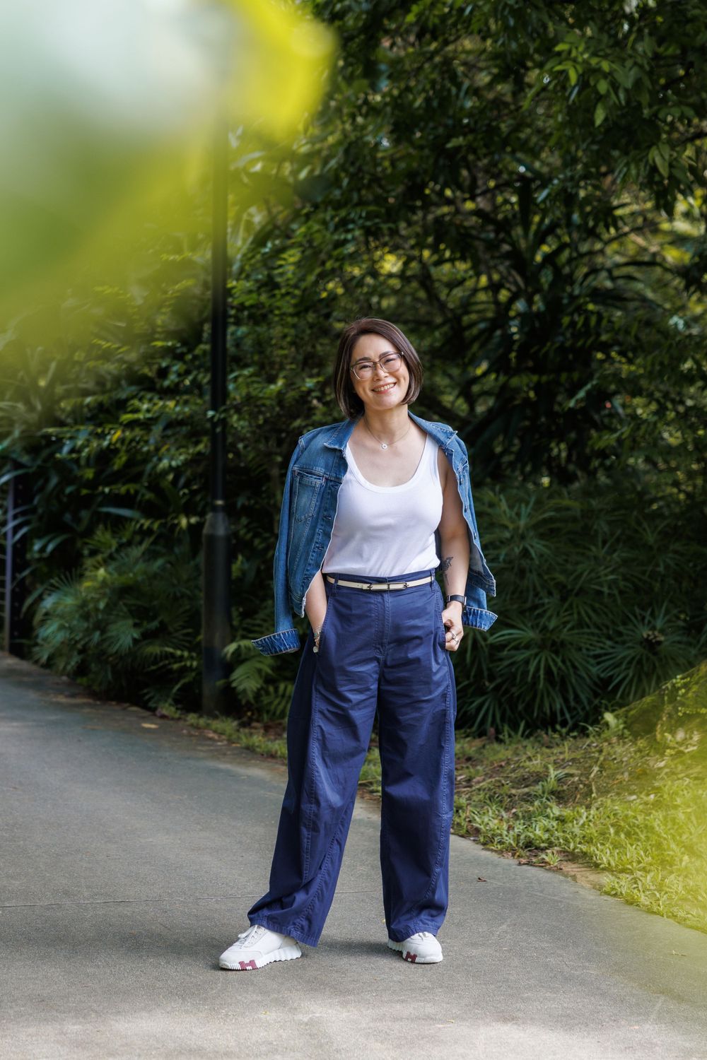 Casual street style featuring denim jacket, white top and wide-leg navy pants on a garden path.