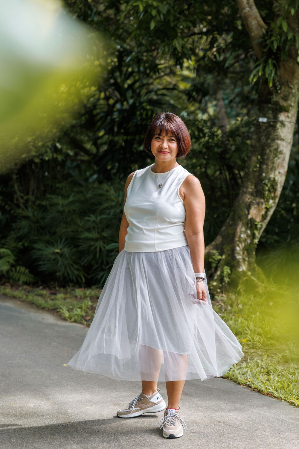 A feminine summer outfit with white top and flowy tulle skirt paired with sneakers on a garden path.