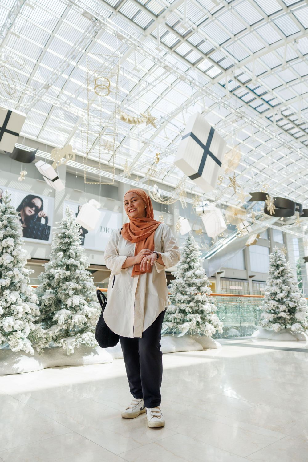 Winter holiday scene with snowy decorations and white Christmas trees in a modern shopping mall interior.