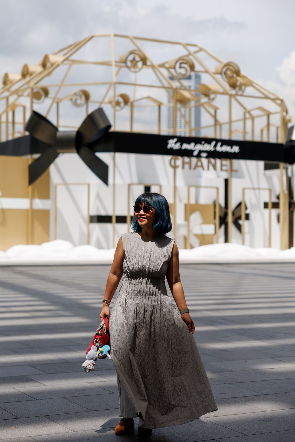 Grey maxi dress outfit posed in front of elegant Chanel display with golden archway and black bow decor.