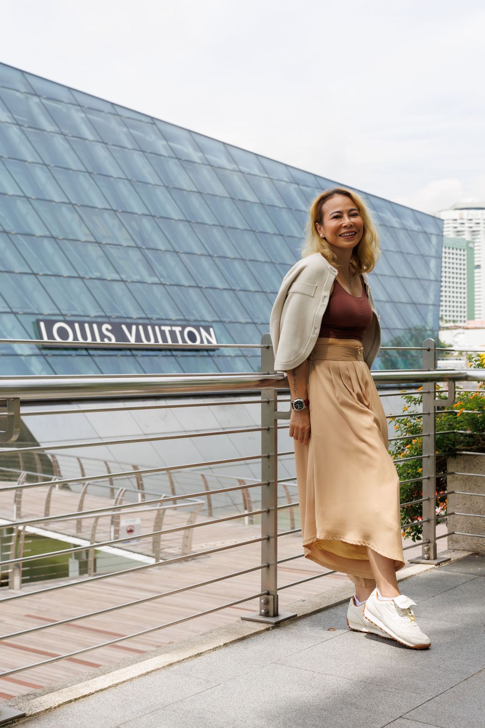 Stylish fashion photo outside Louis Vuitton store featuring cream cardigan, burgundy top and beige skirt with sneakers.