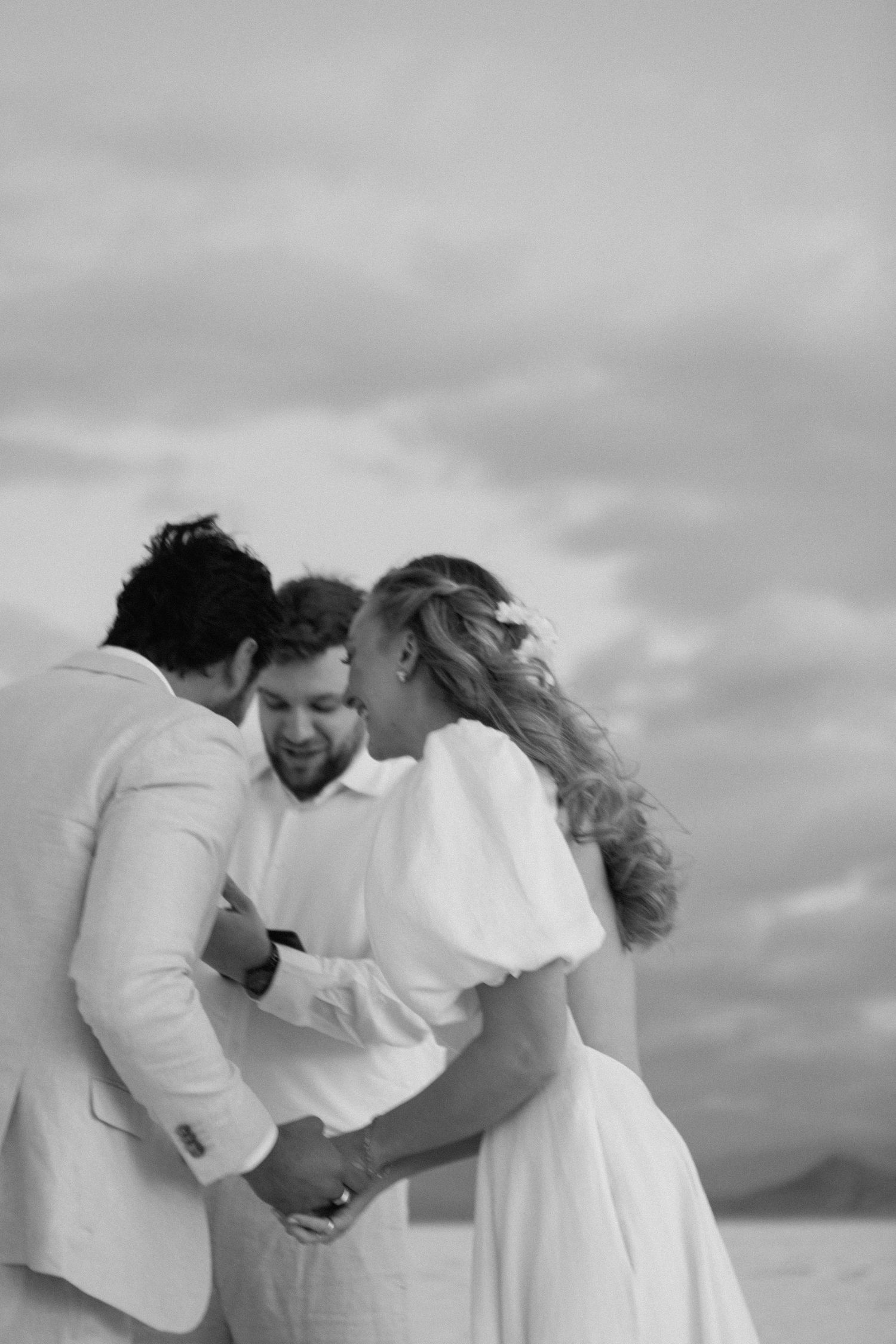 A tender black and white wedding moment captured outdoors with a romantic embrace against a cloudy sky.