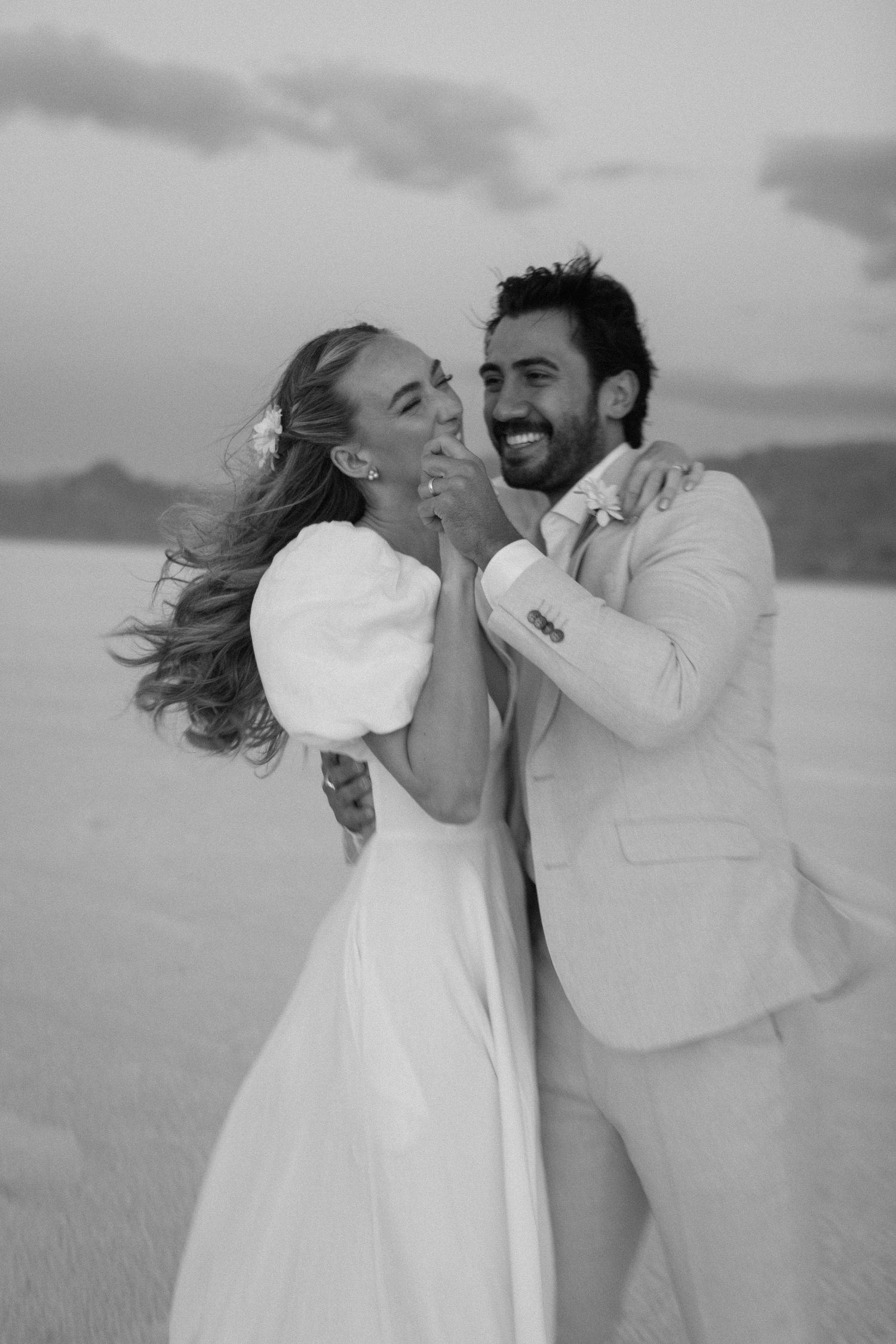 A joyful moment captured in black and white on a salt flat with mountains in the background.